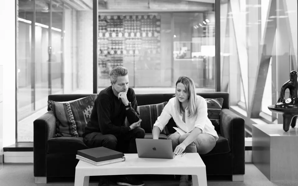 Two people going over work on a laptop in an office lounge